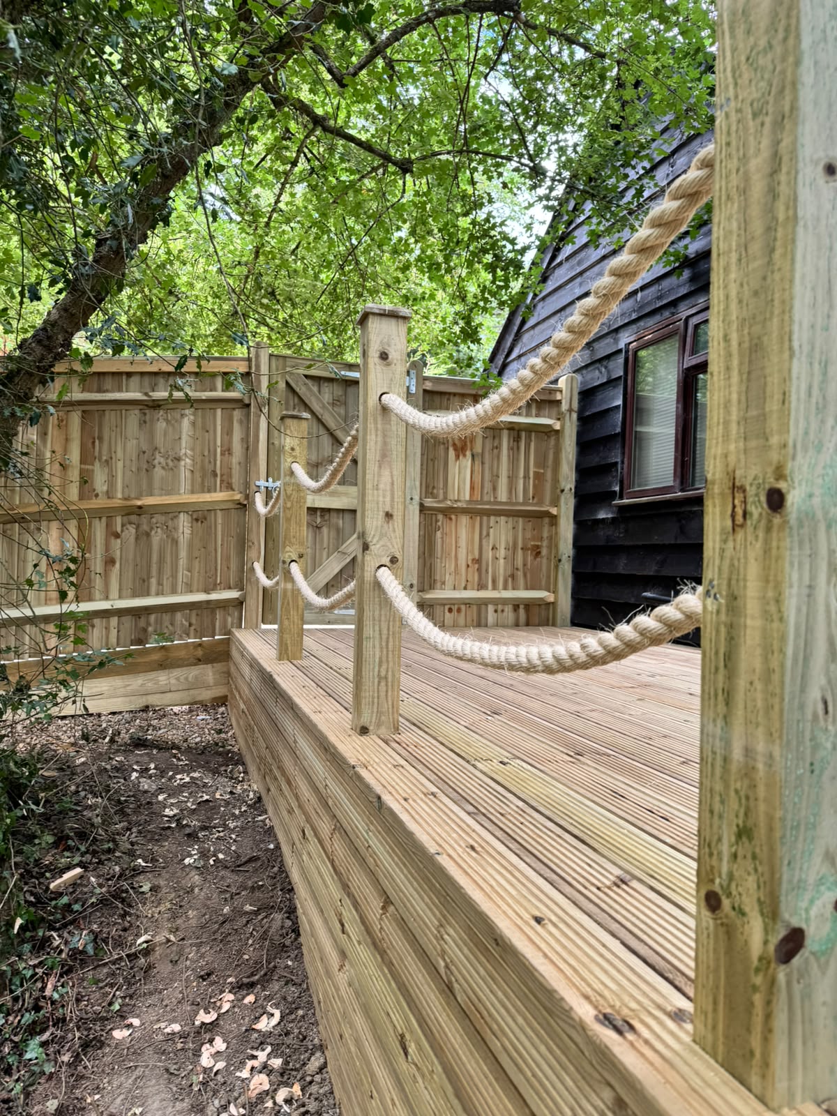 Edge of a raised deck faced with boards and topped with a rope rail