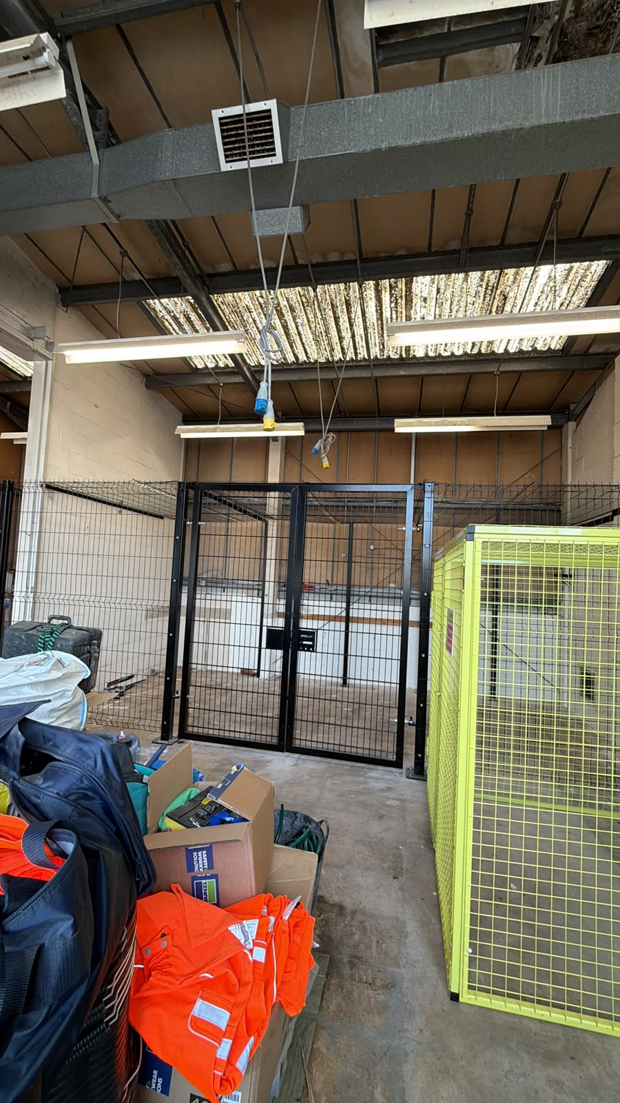 Black welded mesh security cage with lockable double gates fitted inside a workshop