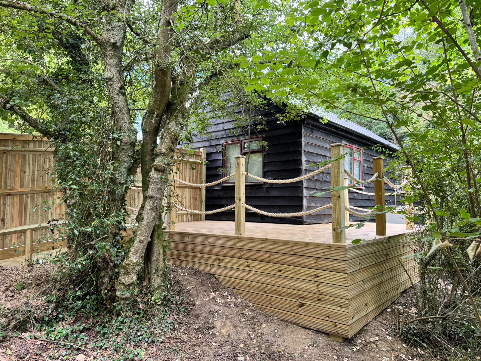 Raised timber deck beside a log cabin framed by trees and rope rails