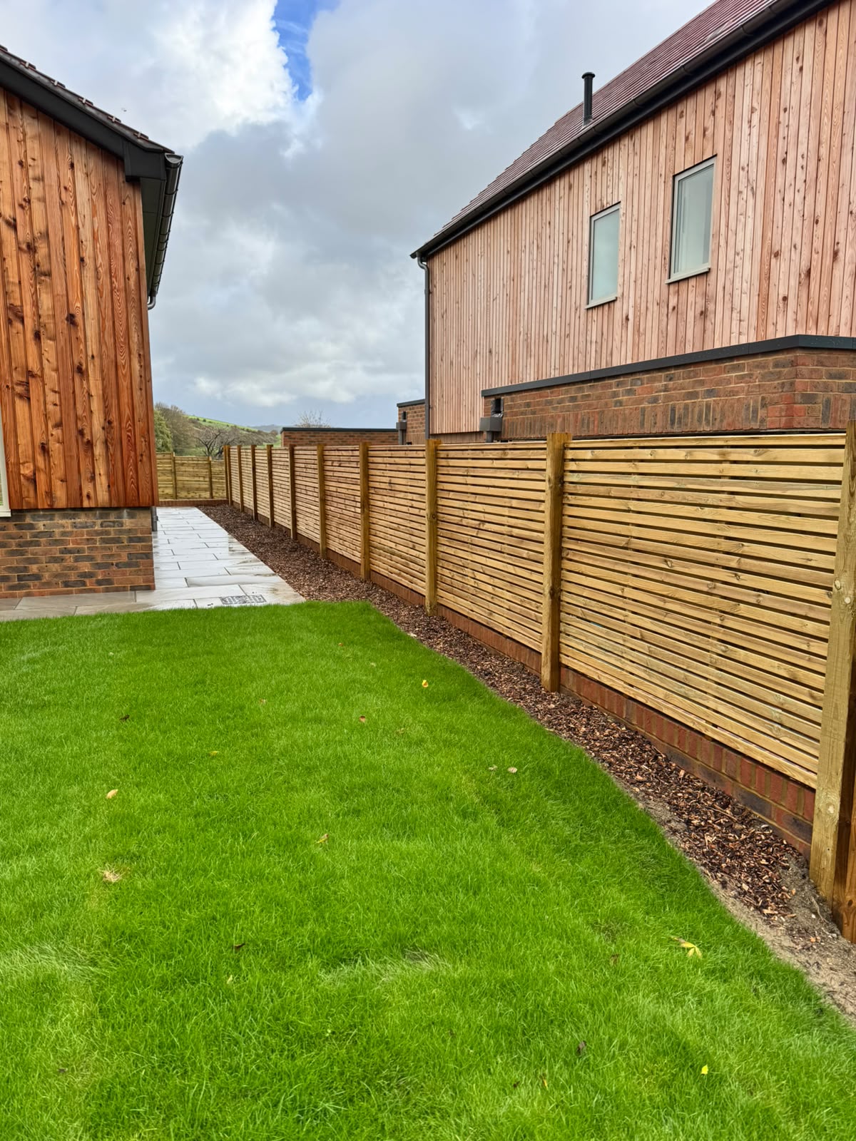 Horizontal slat fencing alongside a new garden with brick edging