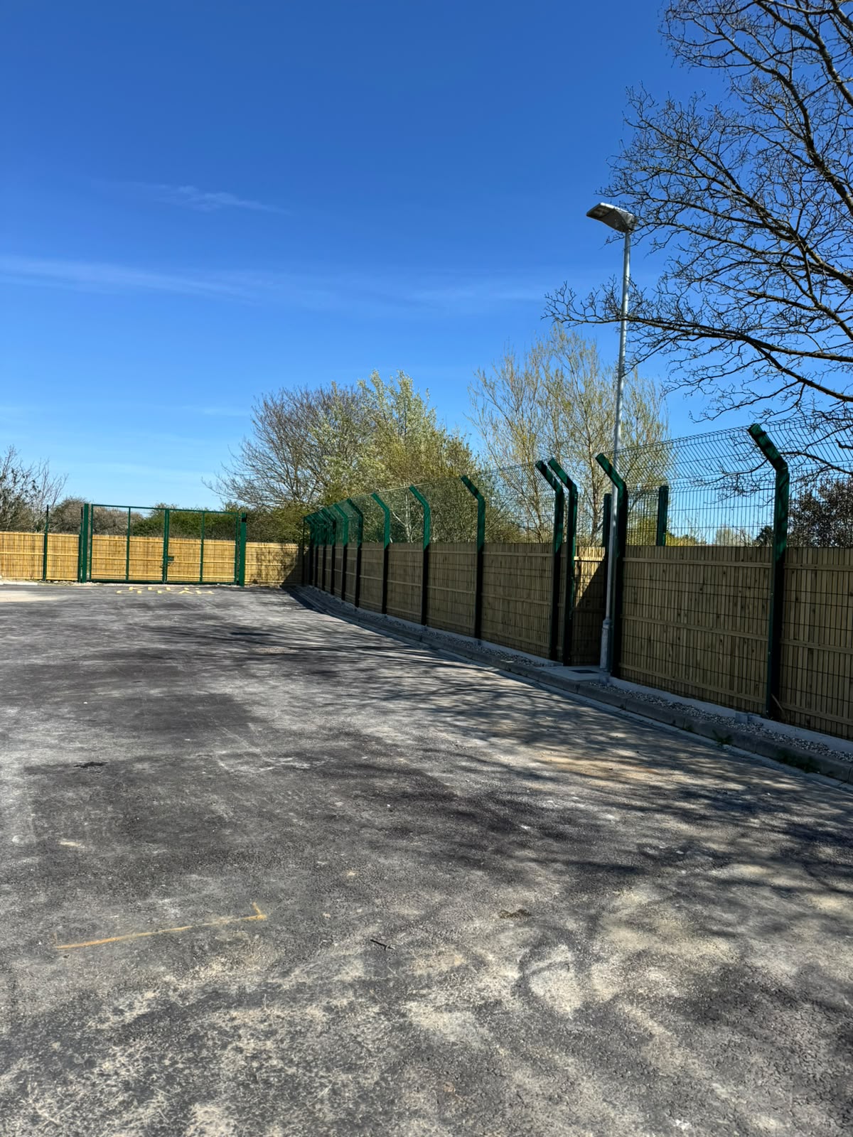 Timber panel fencing topped with green security mesh beside a car park