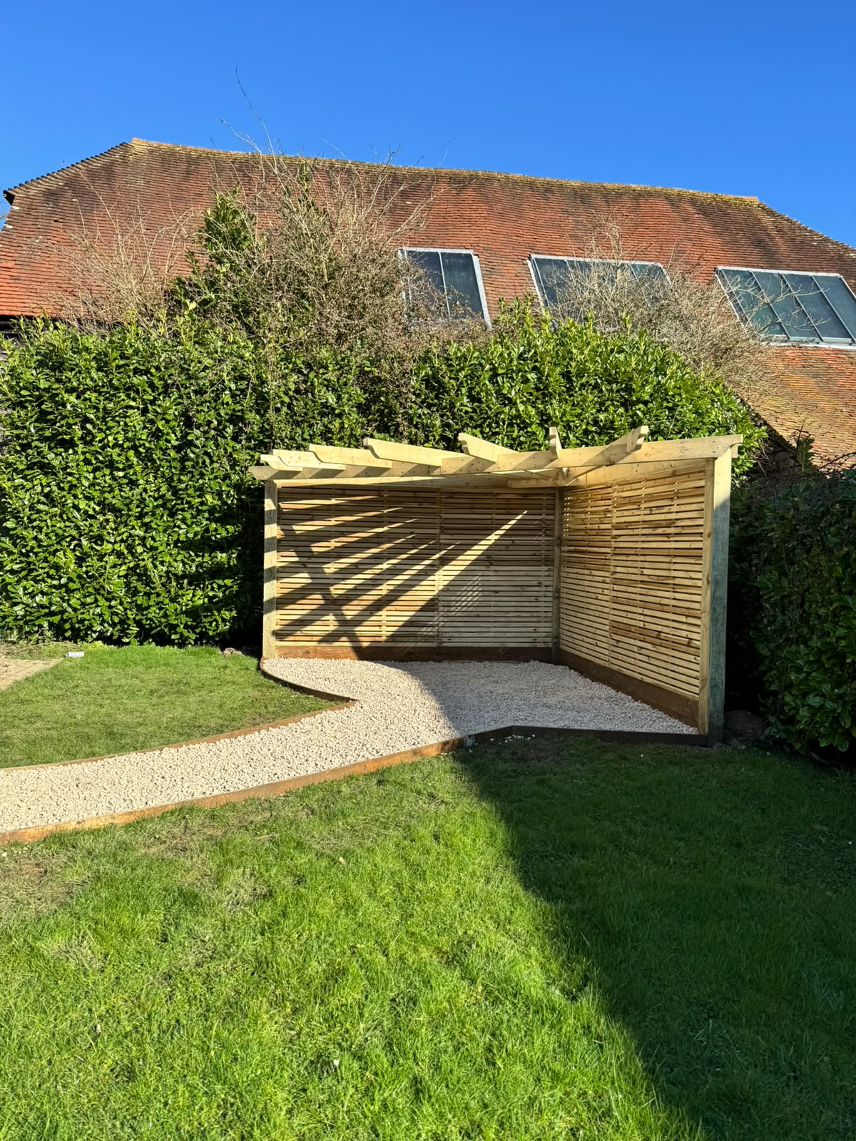 Timber pergola with slatted screens beside a new gravel path