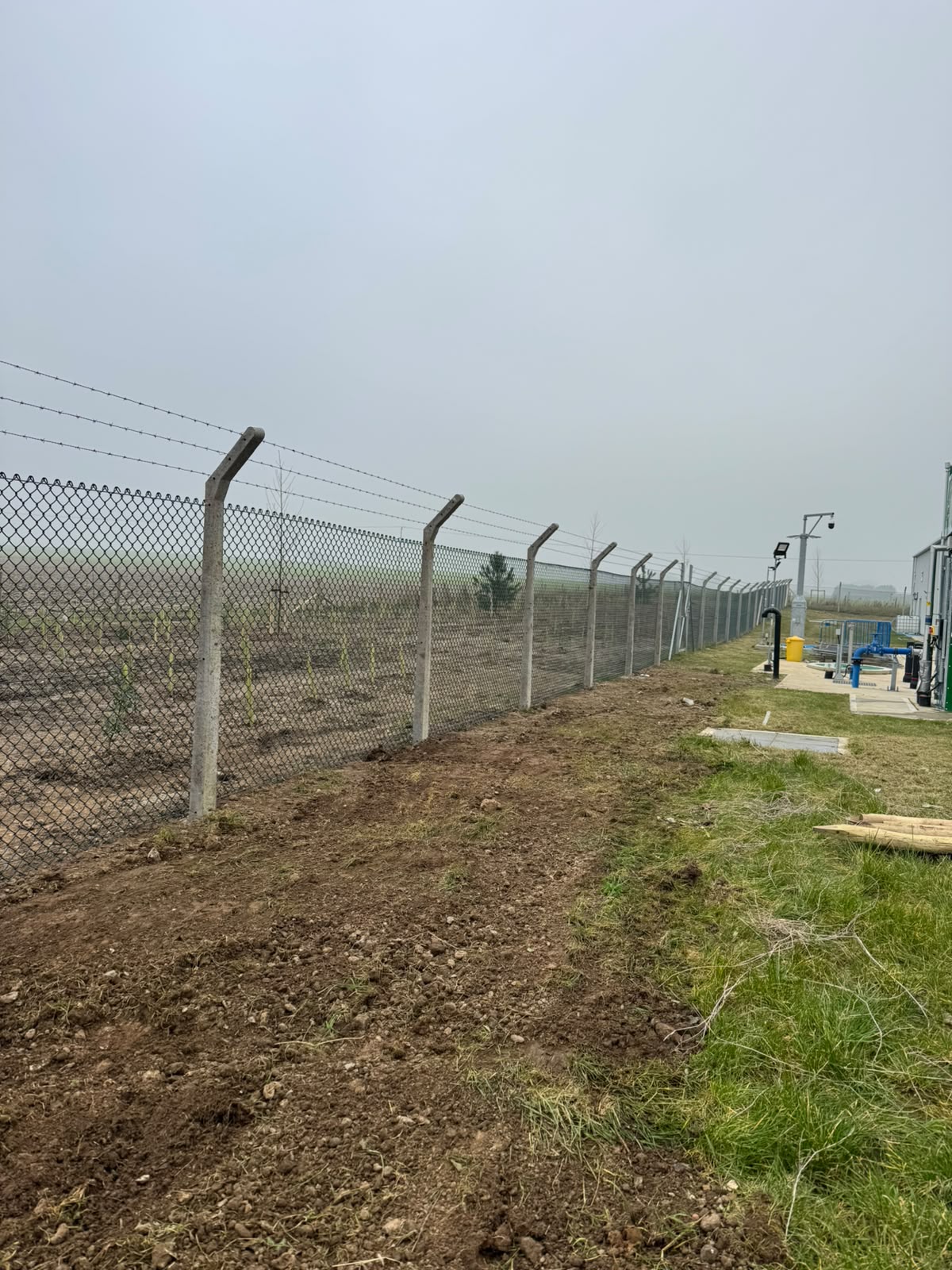 Chain-link perimeter with barbed wire on concrete posts at a utility site
