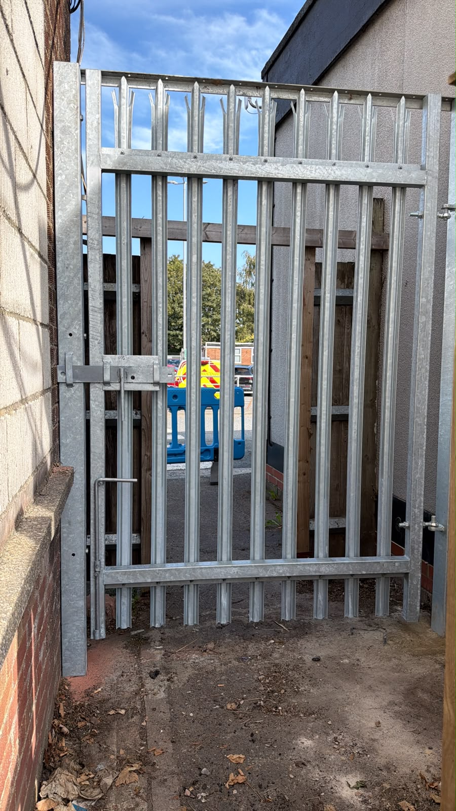 Galvanised palisade gate with pointed pales between two buildings