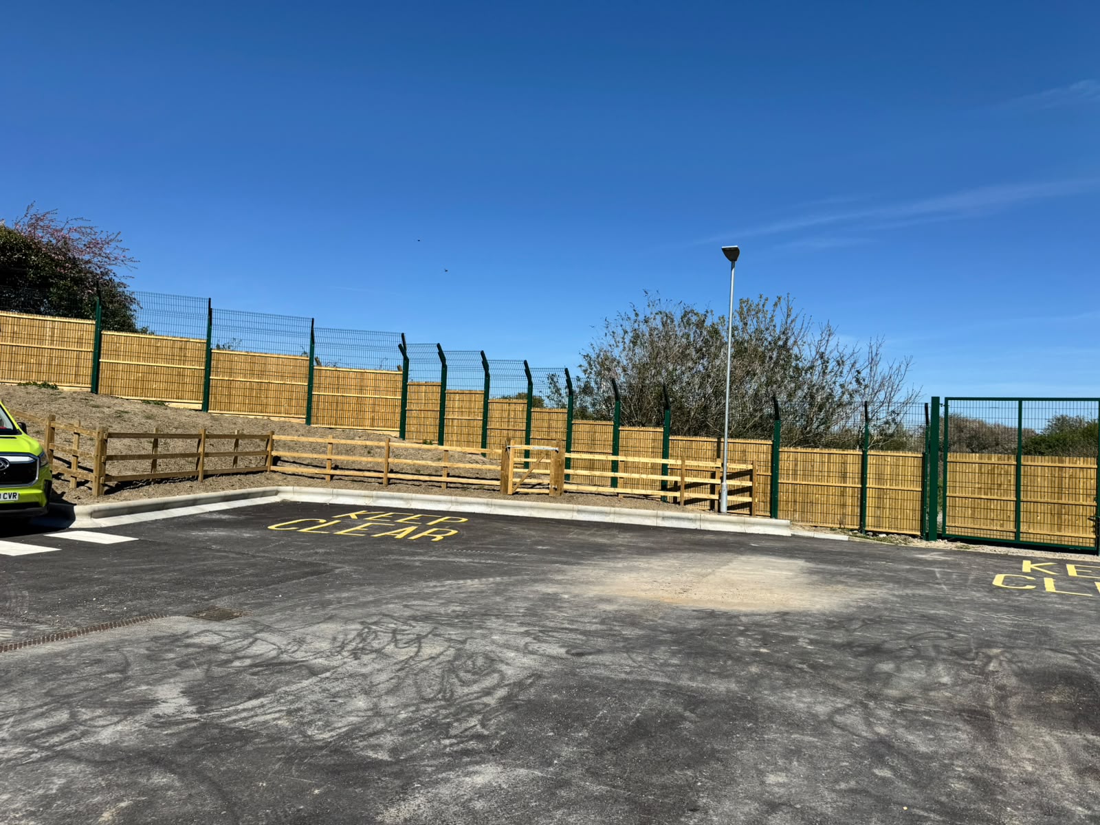 Timber panels with green mesh above and post-and-rail edging at a car park entrance
