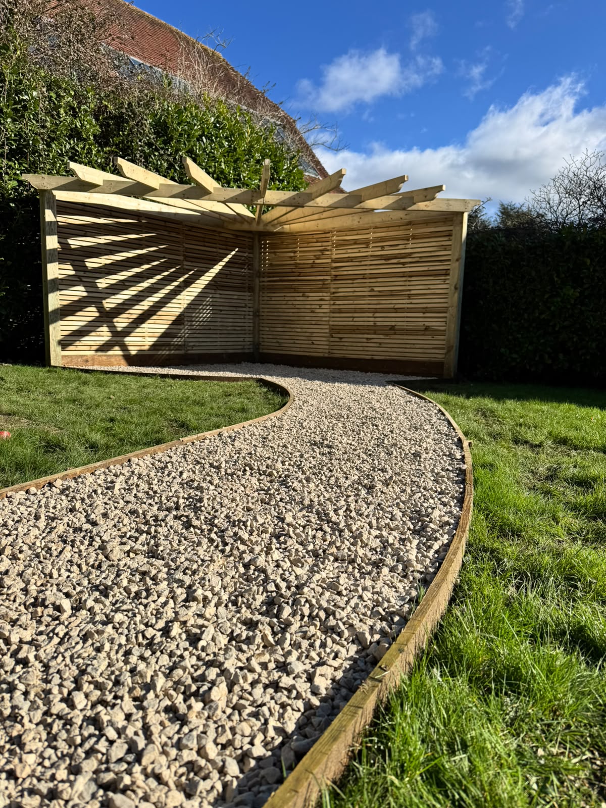 Curved gravel path edged with timber leading to a slatted screen