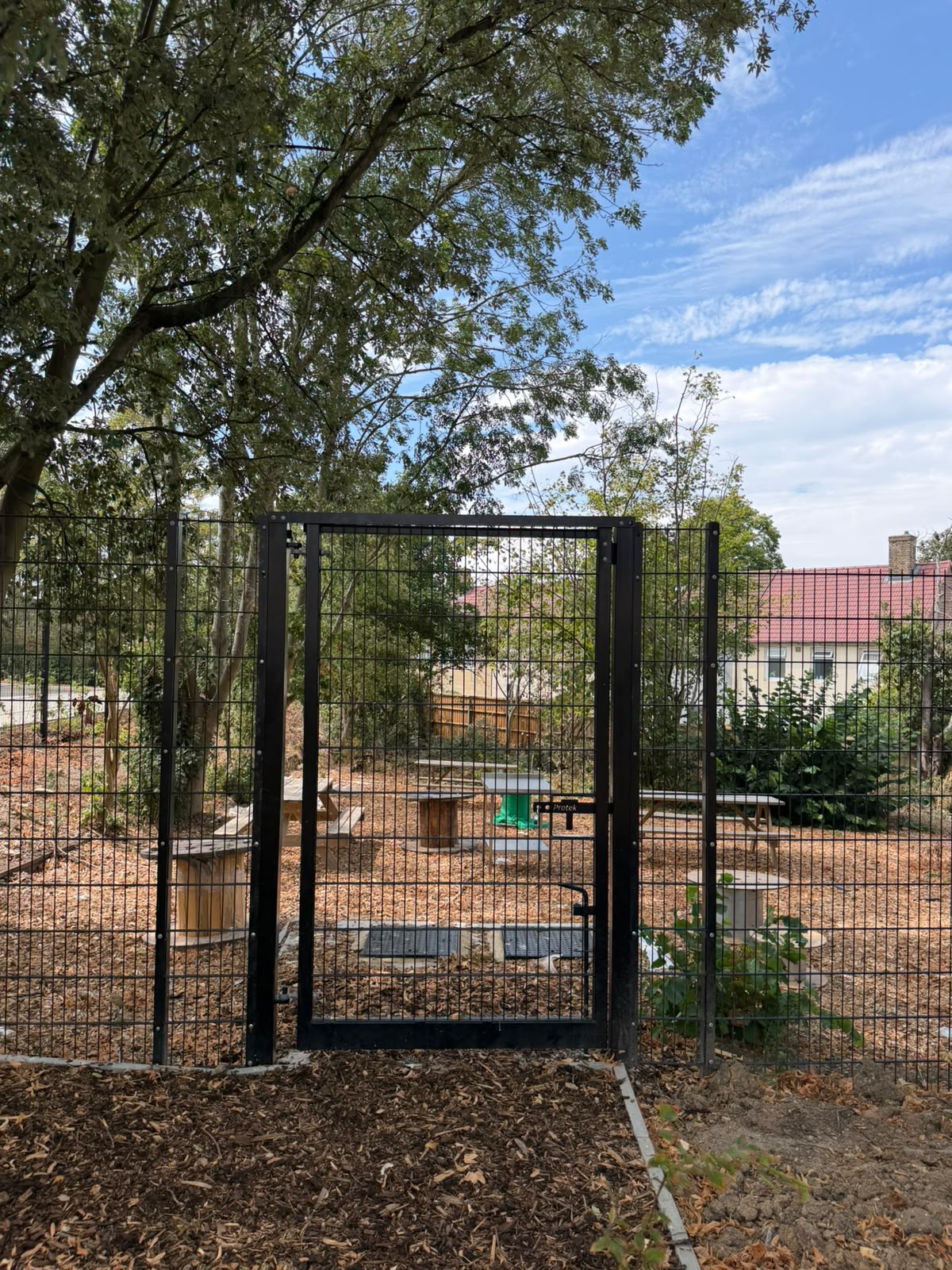 Black weldmesh fence with a lockable pedestrian gate beside garden seating