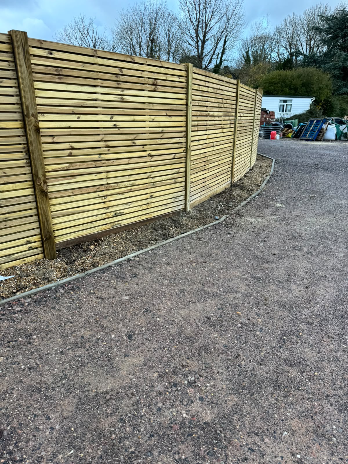 Horizontal slat fencing running along a gravelled driveway