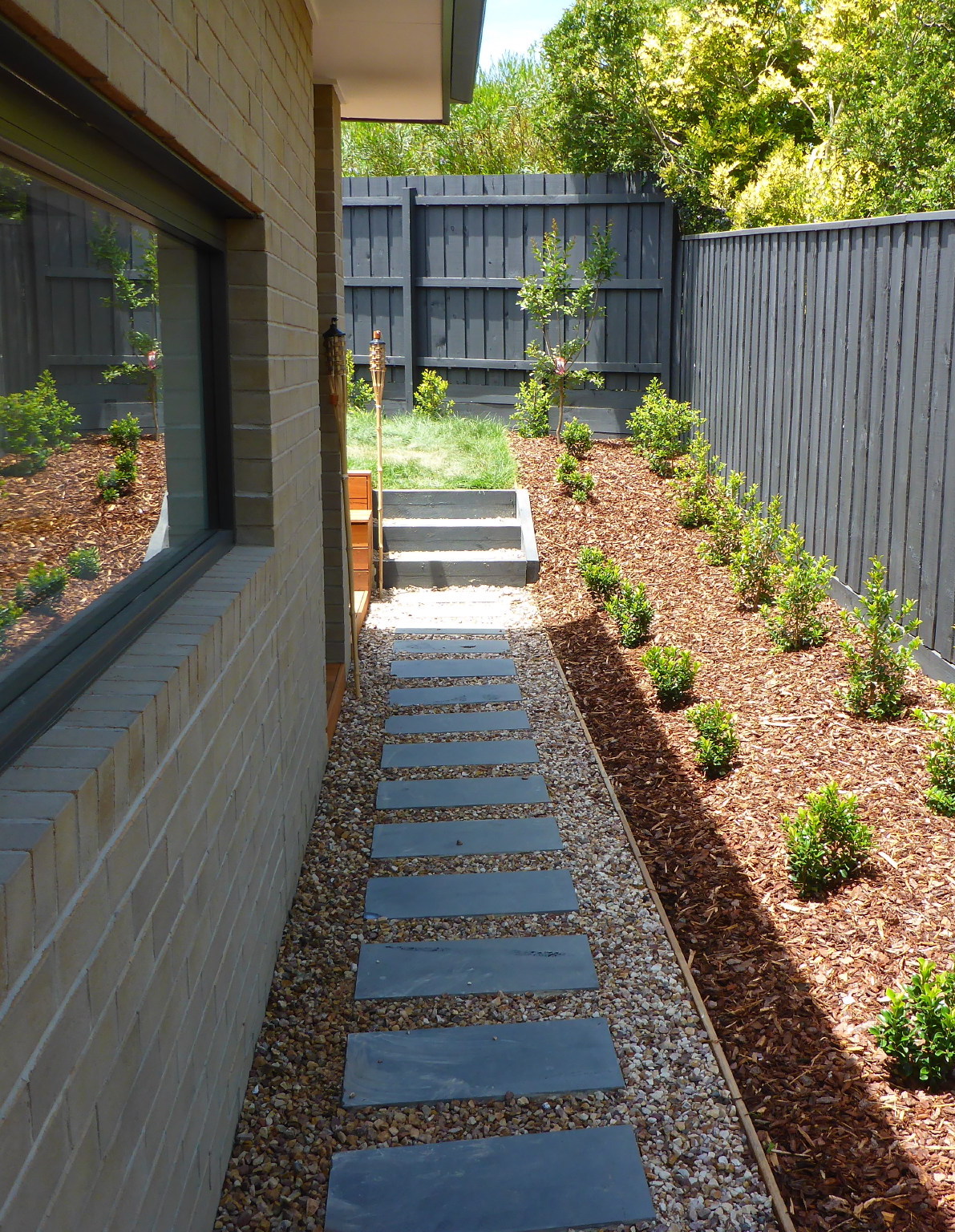 Stepping stone garden path beside planted borders and painted fencing