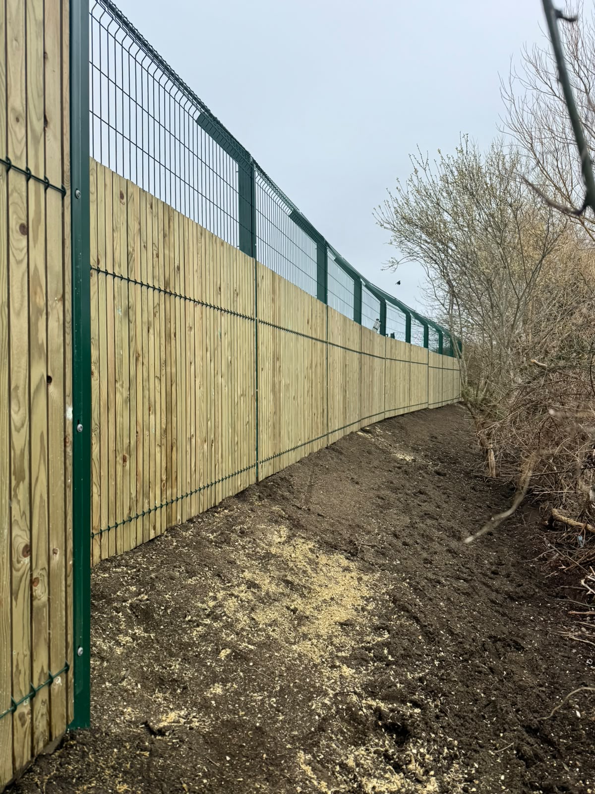 Timber-clad boundary with green security mesh along a public footpath